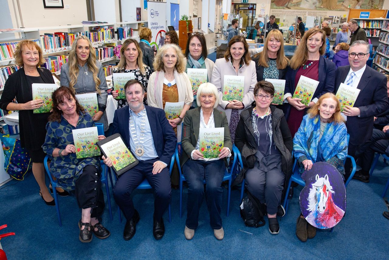 A group of people in a library holding copies of a book titled 